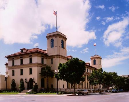 Historical building with American flags, featuring a Mediterranean architectural style, surrounded by trees and a clear blue sky.