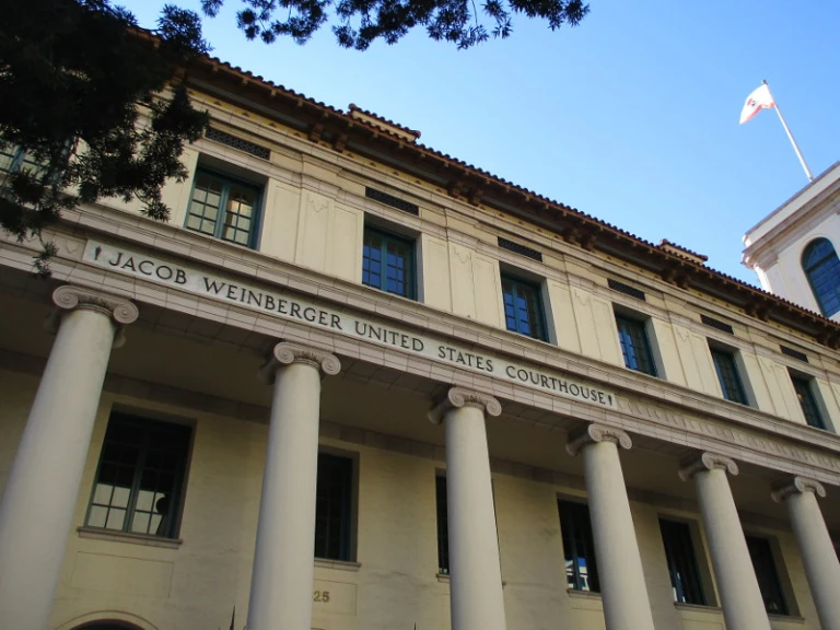Facade of the Jacob Weinberger United States Courthouse, showcasing classical architecture with prominent columns and green windows.
