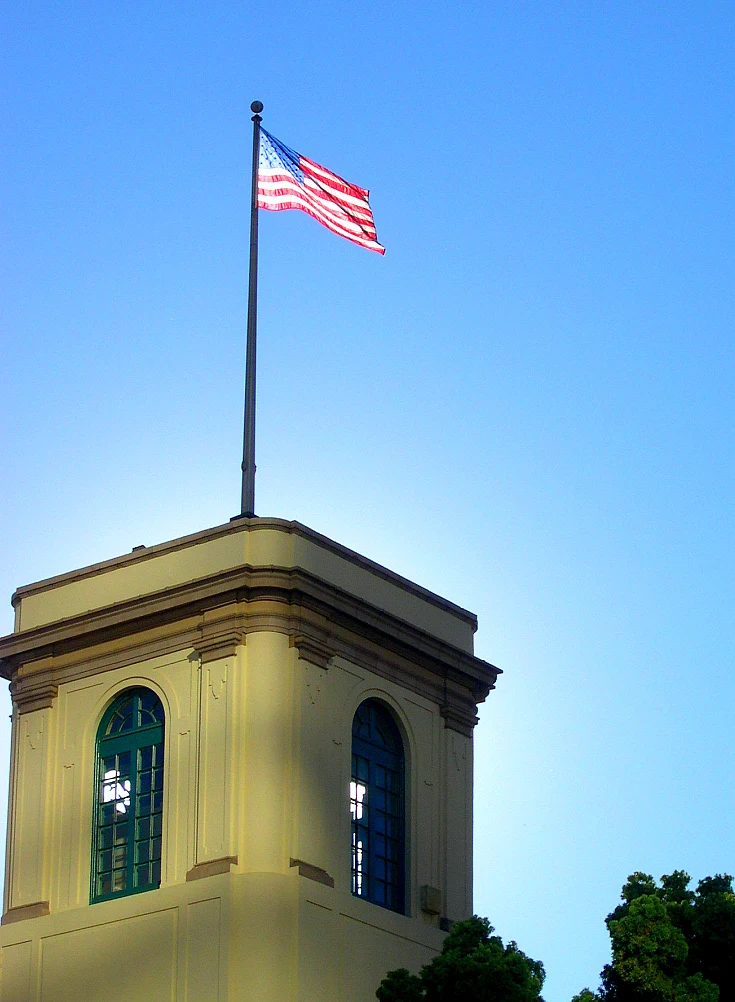 American flag flying atop a historic building, contrasting against a clear blue sky, symbolizing patriotism and national pride.